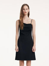 A woman with brown hair wears a black dress with an irregular neckline.